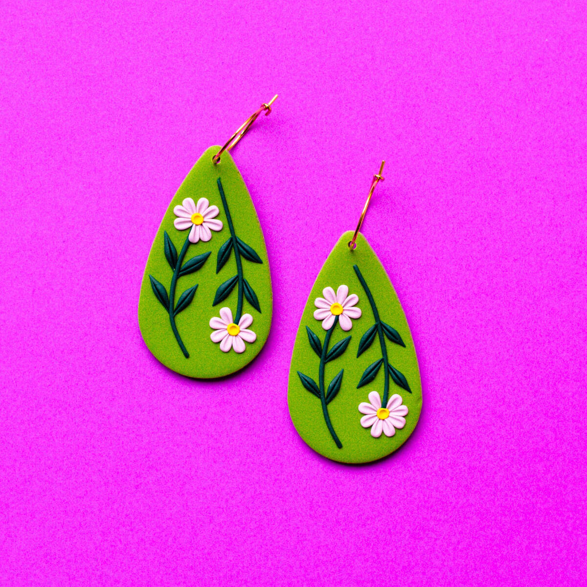 Green teardrop earrings with floral designs on a pink background