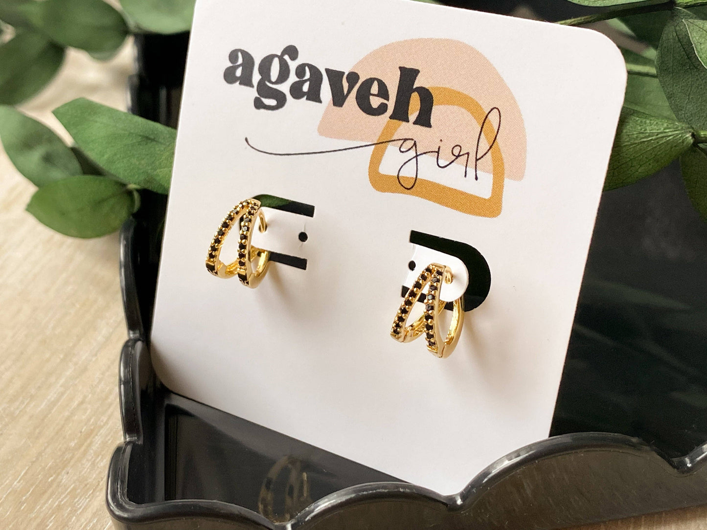 Agaveh Girl Blair Hoops displayed on a branded card in a dark scalloped tray with greenery, showing the double gold-plated hoop design with black stone detailing. Made in Canada.