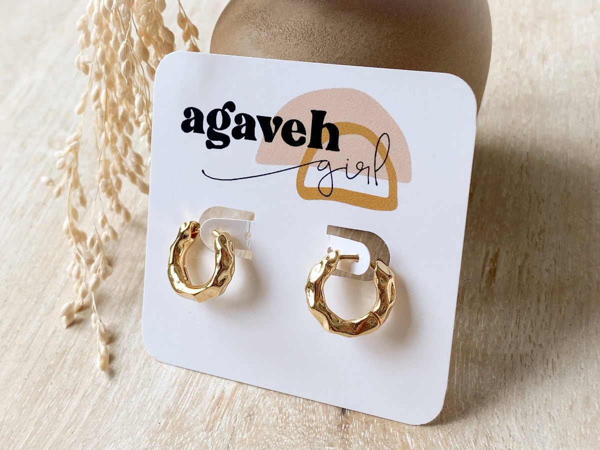 Agaveh Girl Greece Hoops, made in Canada, with a dimpled gold finish on a white branded display card beside dried stems on pale wood.
