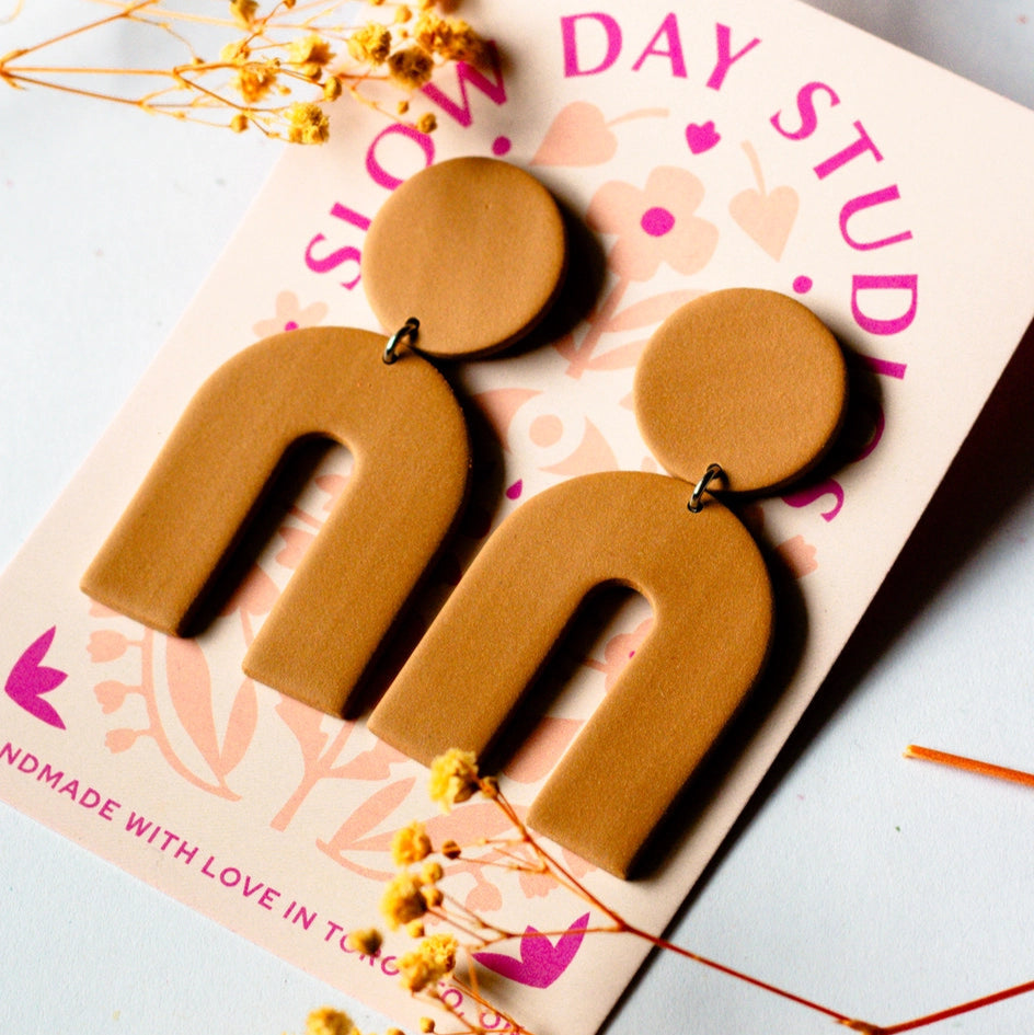 toffee brown arch statement earrings from slow day studios on a plain background with dried floral accents