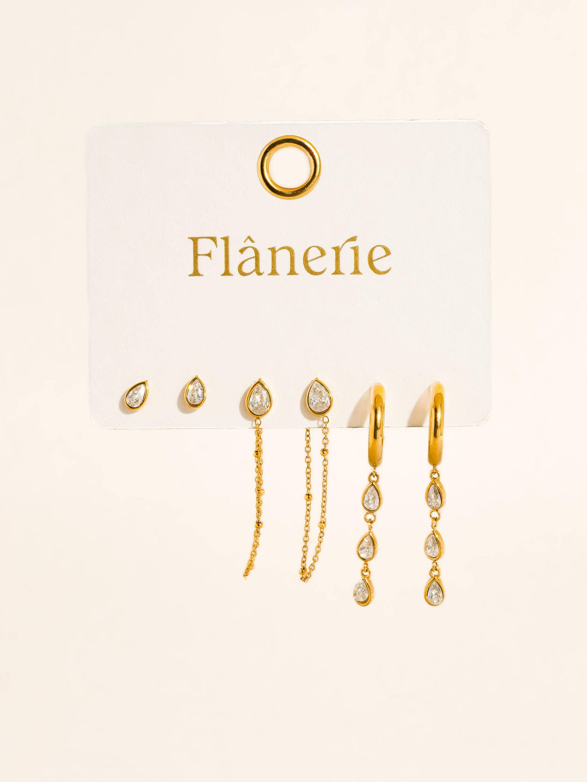 Finley earring set by Flânerie by MAIQ featuring gold teardrop studs, chain studs and hoop dangles with clear stones on a cream branded display card.