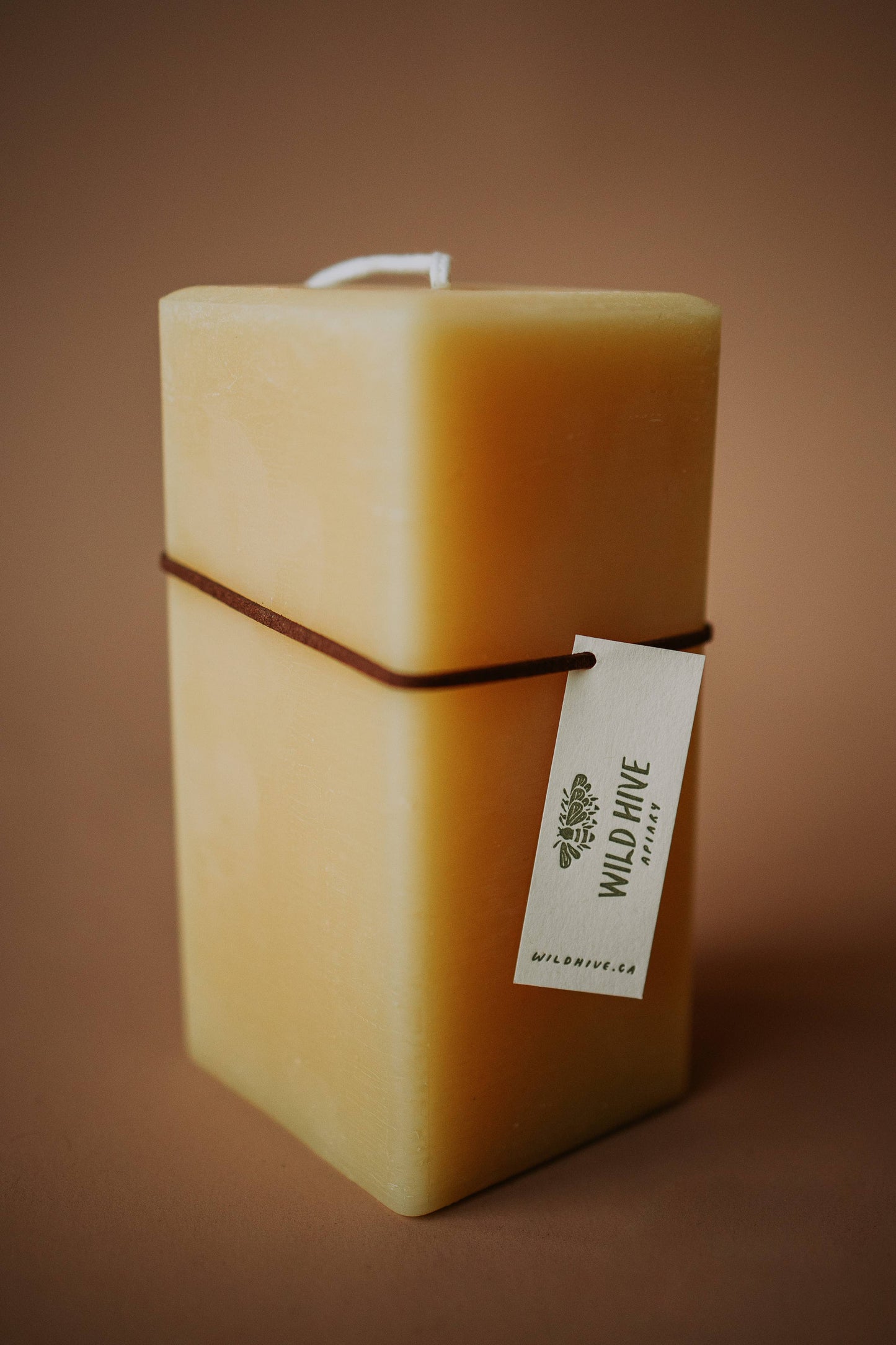 Wild Hive Apiary Large Square Beeswax Pillar Candle in warm golden hue, hand-tagged and cord-wrapped, ready to gift. Made in Alberta, Canada.