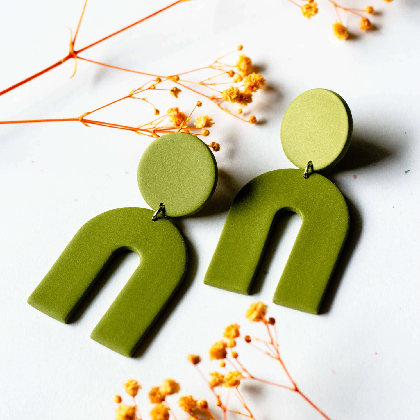 Green U-shaped earrings on a white background with dried flowers.