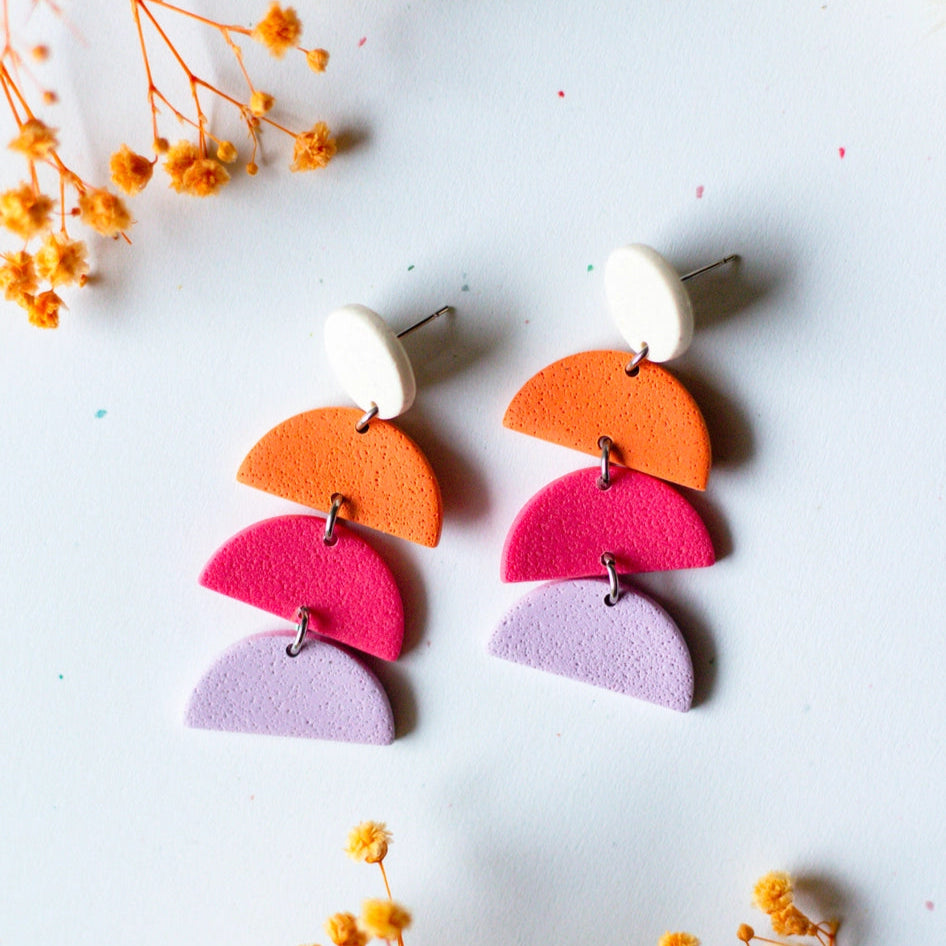 Colorful geometric earrings on a light surface with small yellow flowers.