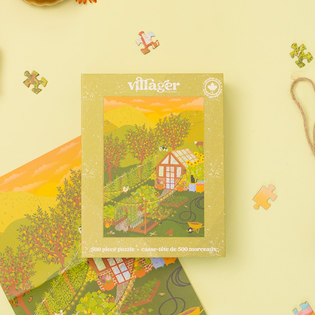 Villager Puzzles’ Hobby Farm 500-piece puzzle in an olive-green box featuring garden and greenhouse artwork, with a matching poster and loose pieces on a pale yellow background. 