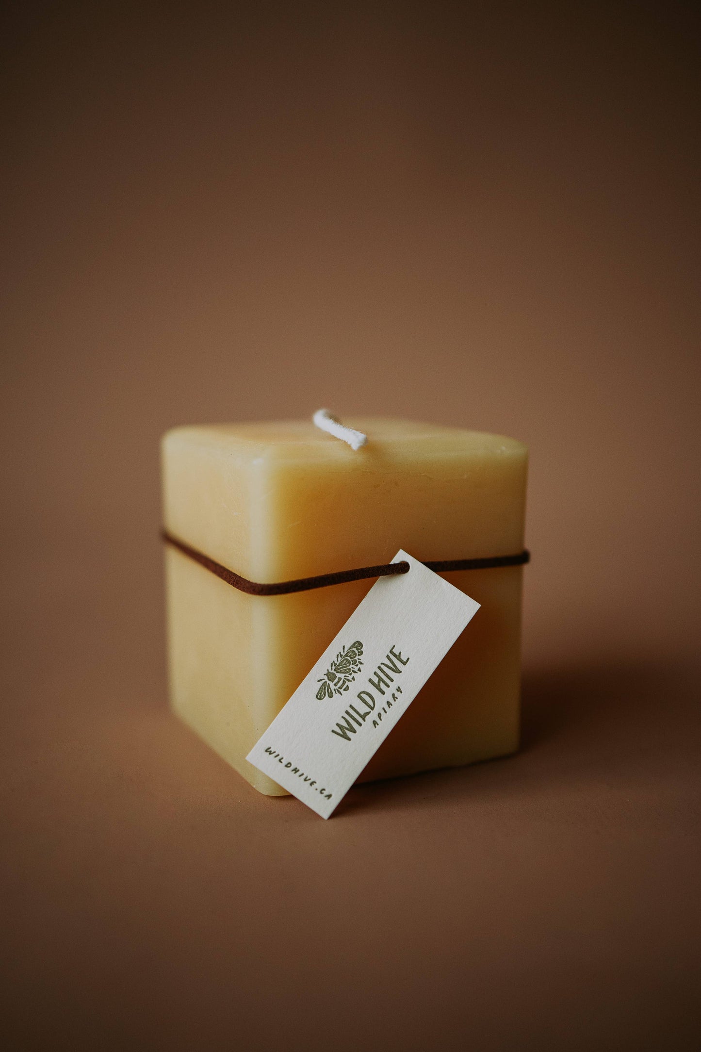 Wild Hive Apiary Small Square Beeswax Pillar Candle in natural golden beeswax, cord-tagged and styled for a modern tablescape. Made in Alberta, Canada.