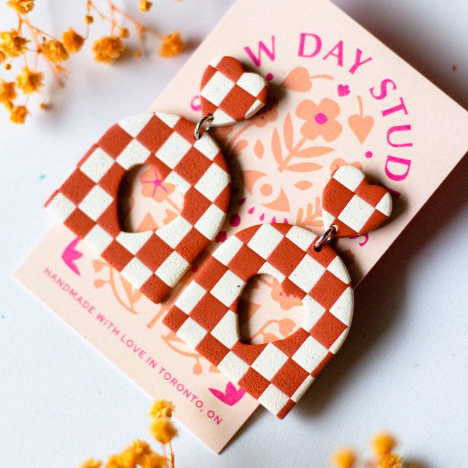 Checkered earrings on a 'Slow Day Studios' card with dried flowers around