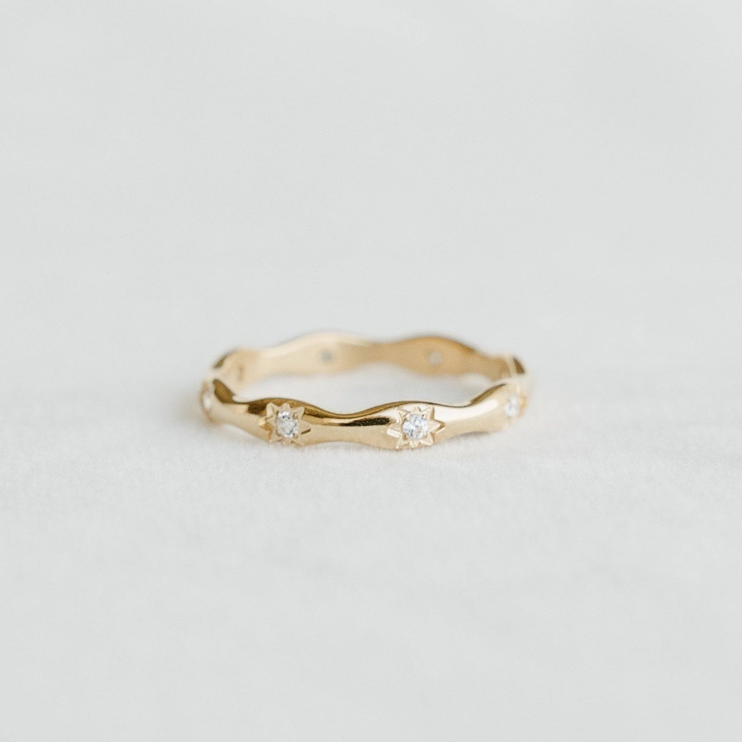 Petite Gold Aurora Band in 18k gold PVD stainless steel, a wavy ring with two star-set stones photographed on a soft white surface — a dainty stackable ring for everyday wear. Made in Canada.