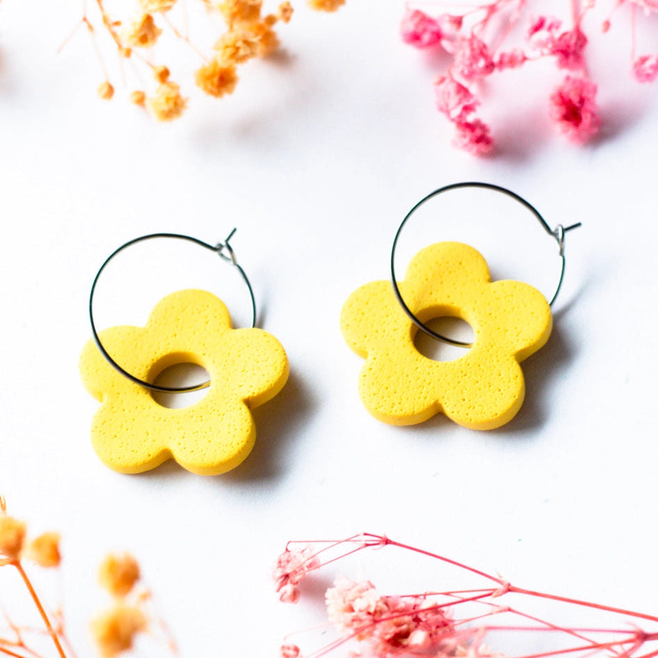Yellow flower-shaped earrings on a white background with dried flowers.