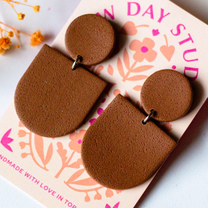 Brown earrings on a decorative card with floral designs and text.