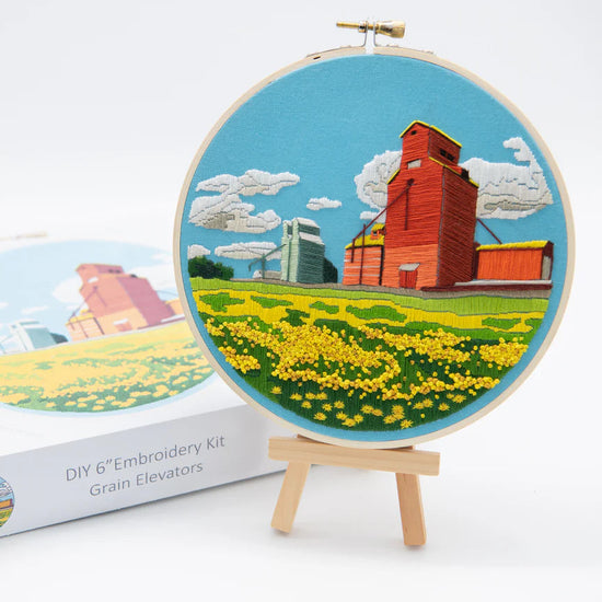 DIY 6" Embroidery Kit | Blue Background with a red grain elevator, a smaller green grain elevator further behind, grain field in front, a classic Canadian prairies scene.