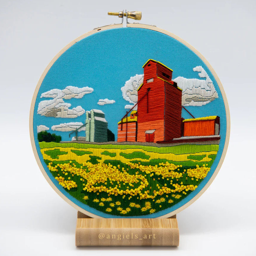 DIY 6" Embroidery Kit | Blue Background with a red grain elevator, a smaller green grain elevator behind, grain field in front, a classic Canadian prairies scene.