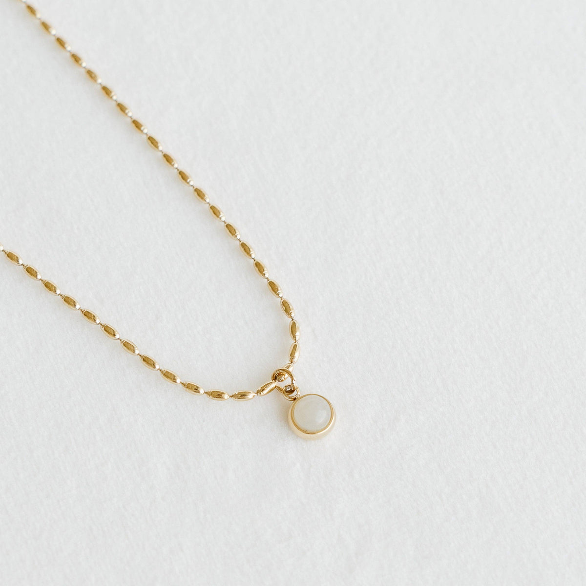 Petite Gold Opal Necklace, made in Alberta, Canada, with a round milky-white pendant in a gold setting on a delicate gold chain against a white background. 