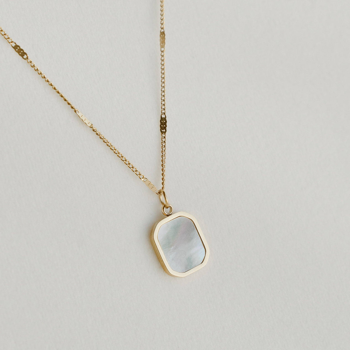 Petite Gold Aurelia Necklace, made in Alberta, Canada, with a rounded rectangular mother-of-pearl pendant framed in gold on a textured gold chain against a pale background.
