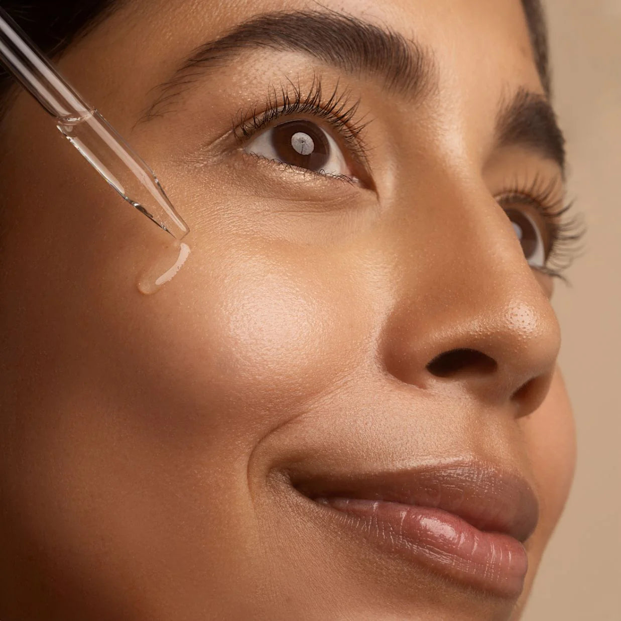 Close-up of a woman applying skincare product to her face with a dropper.