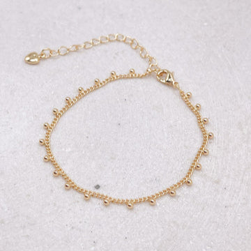 Gold bracelet with small beads on a light gray background