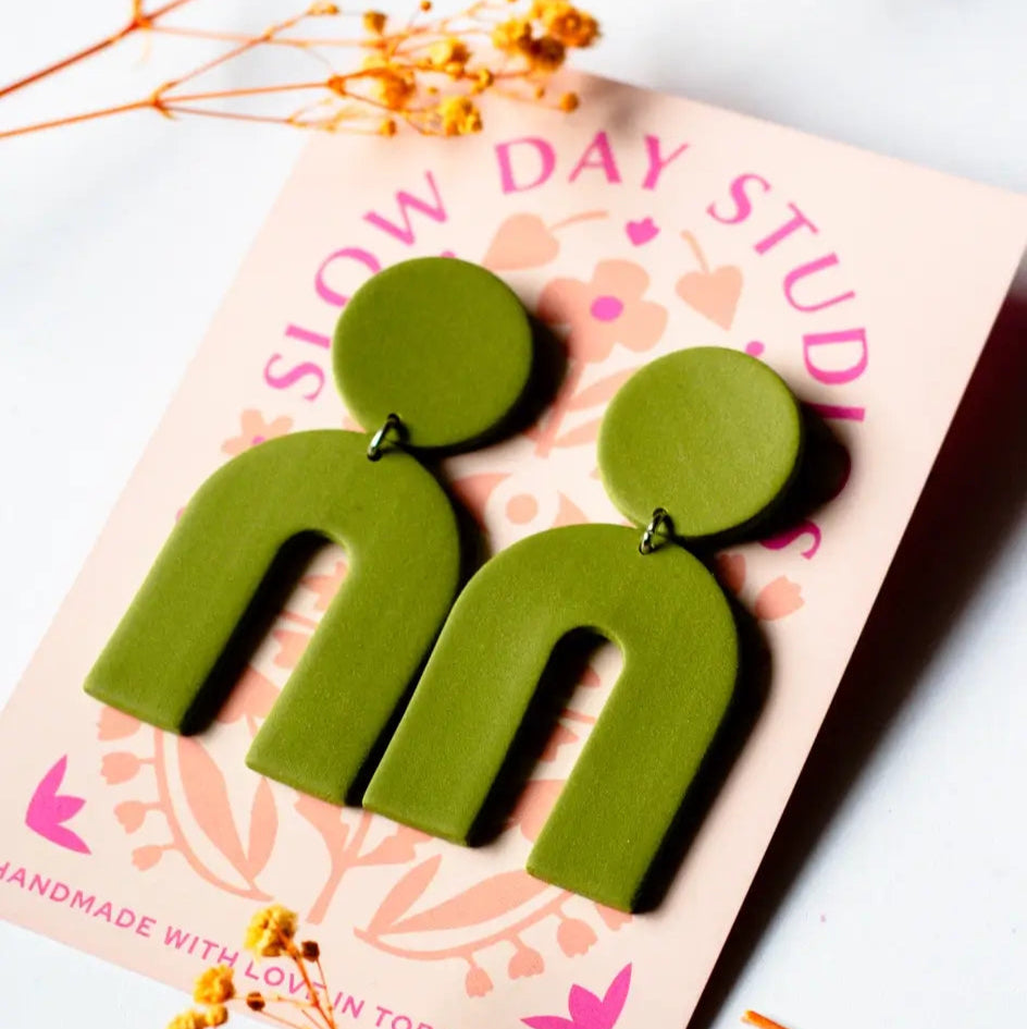 Green arch-shaped earrings on a pink card with 'Slow Day Studio' branding.