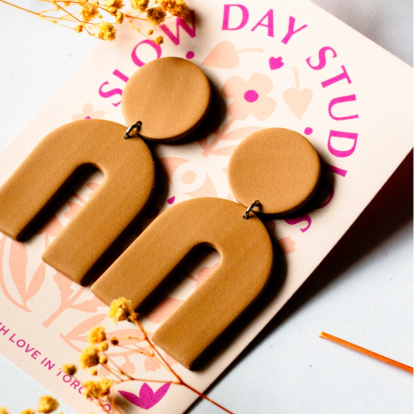 toffee brown arch statement earrings from slow day studios on a plain background with dried floral accents