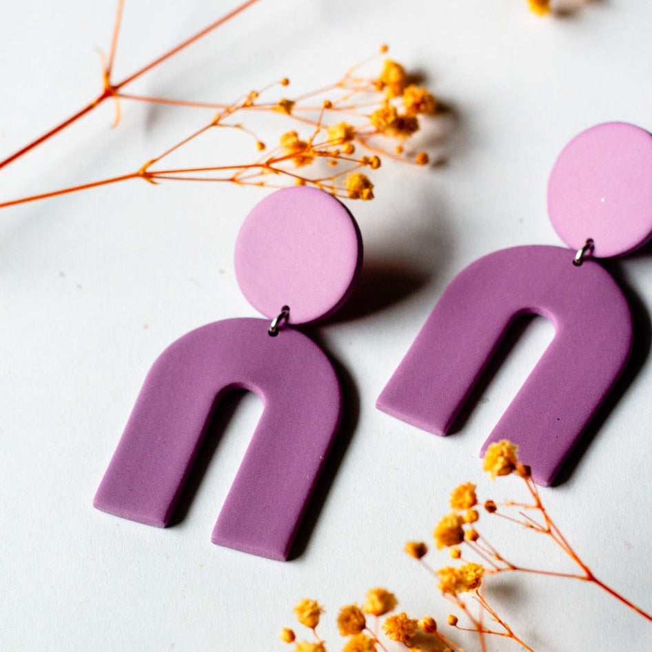 Purple U-shaped earrings on a white background with dried flowers.