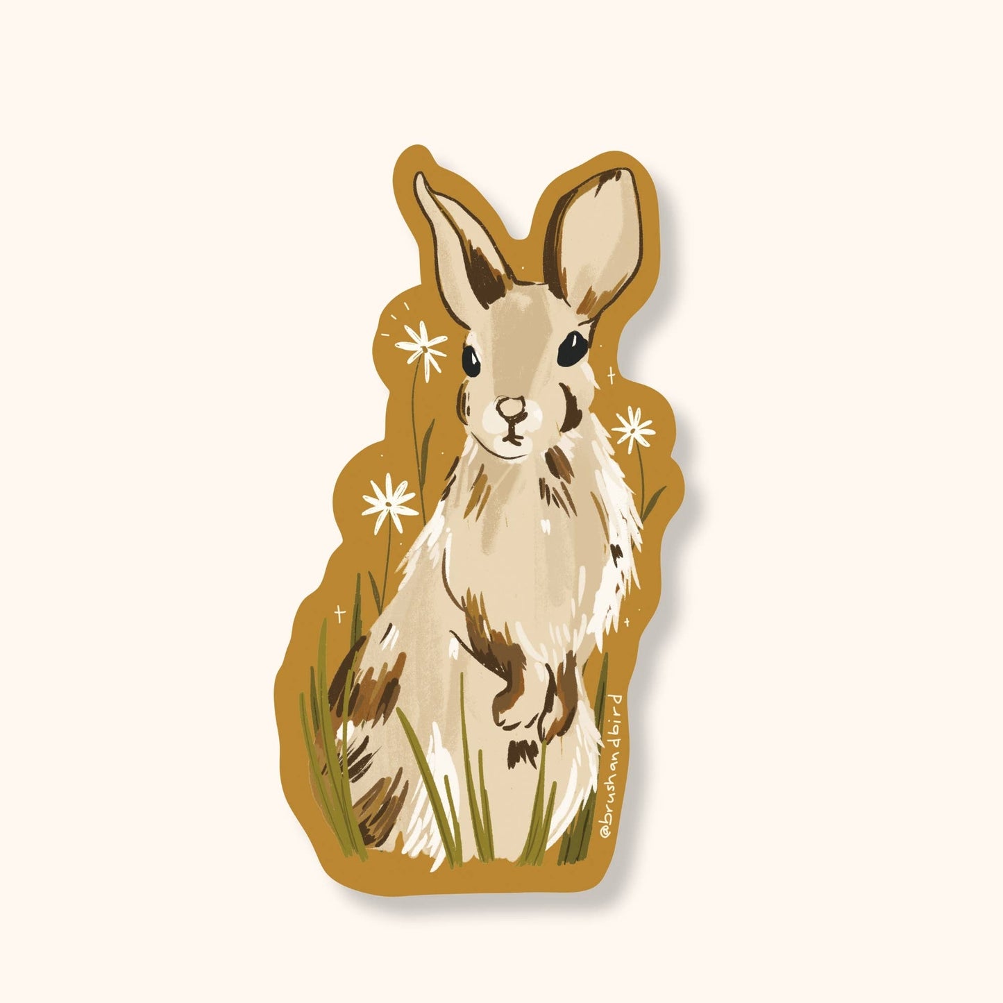Brush & Bird's Rabbit die-cut sticker featuring a detailed illustrated cottontail bunny with cream and brown tones, sitting in green grass with white daisy details on a golden amber background — a nature-inspired sticker perfect for cottagecore and woodland aesthetics.