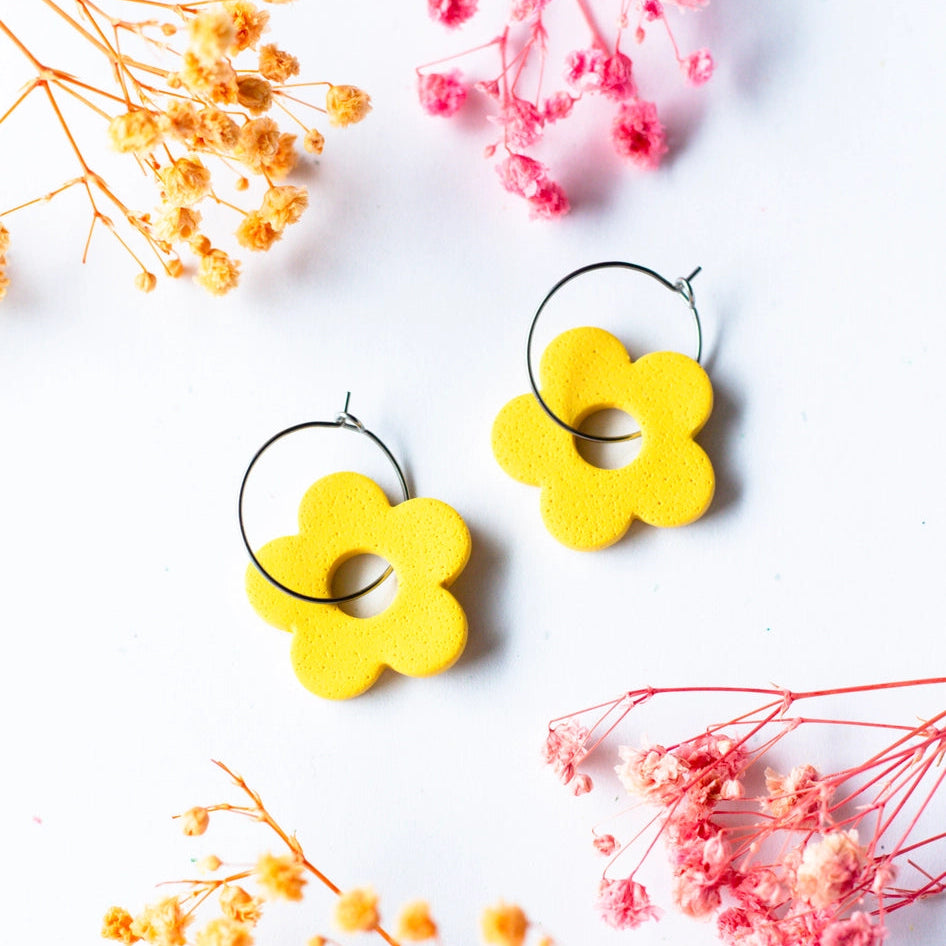 Yellow flower-shaped earrings on a white background with dried flowers.