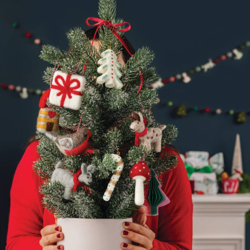 Person holding a small decorated Christmas tree with ornaments against a festive background.
