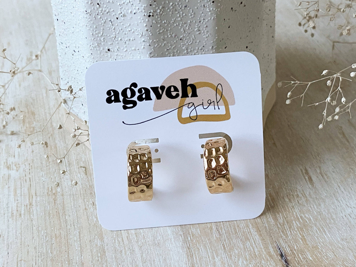 Agaveh Girl Dottie Hoops, made in Alberta, Canada, with a hammered gold finish on a white branded card beside dried white flowers and a textured pot. 