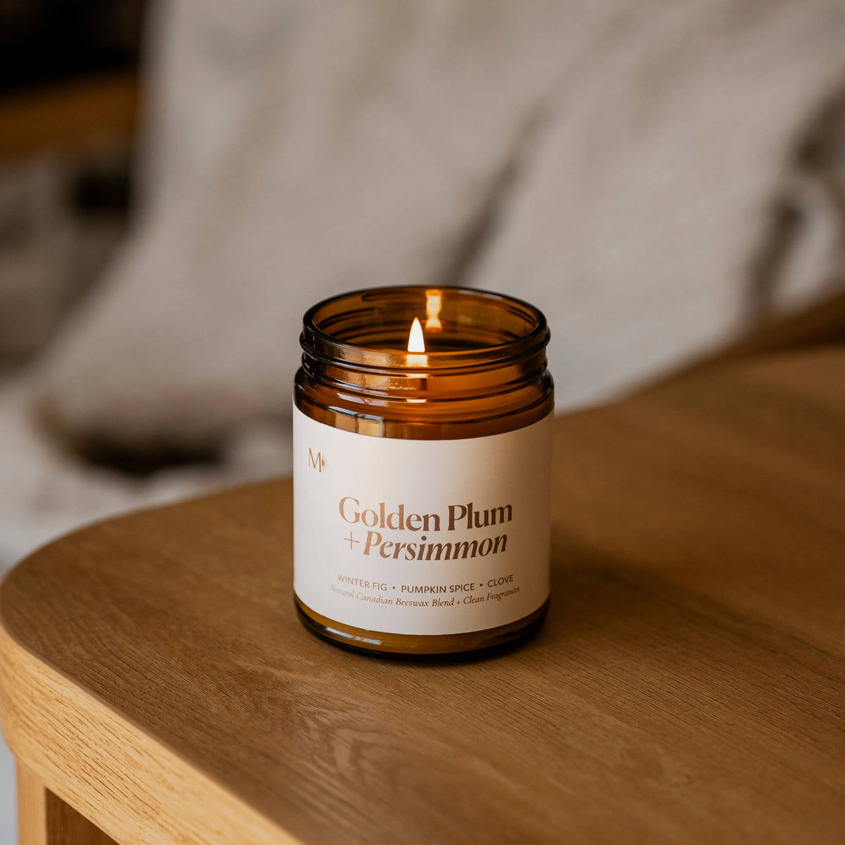 Golden Plum + Persimmon candle by Misiyo Candle Co, small batch handmade in Alberta. Lifestyle photo with the candle lit on a wooden surface with a cozy blanket in the background.