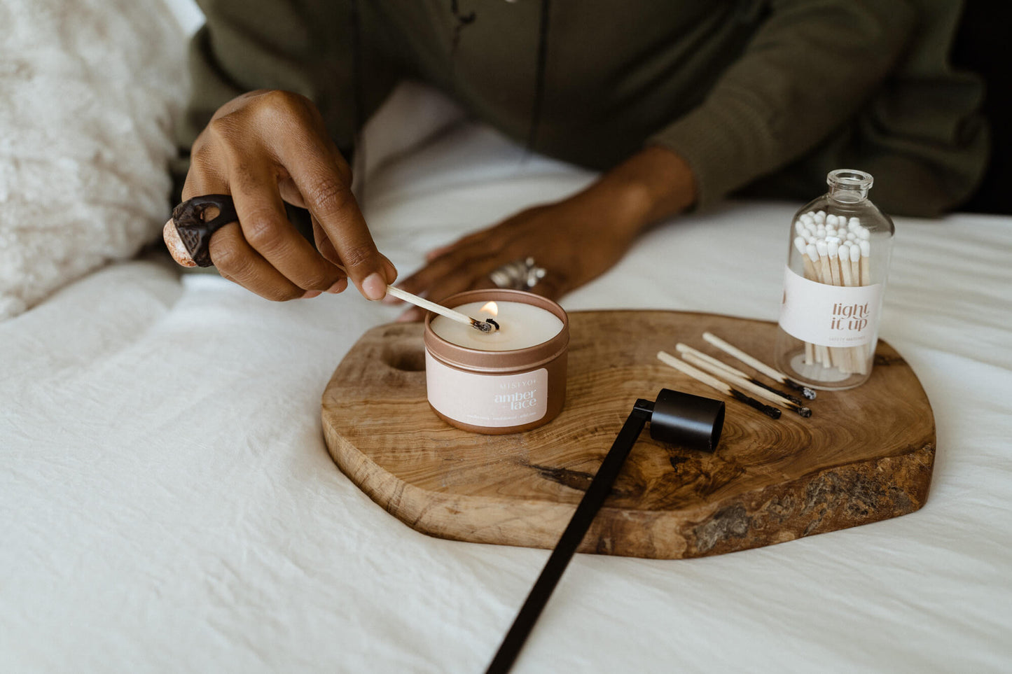 Person lighting a candle on a wooden tray with matches and other items.