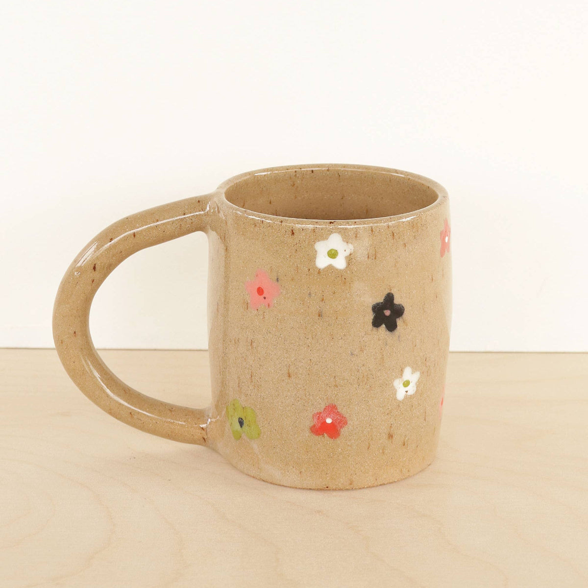 Beige ceramic mug with colorful flower patterns on a beige surface