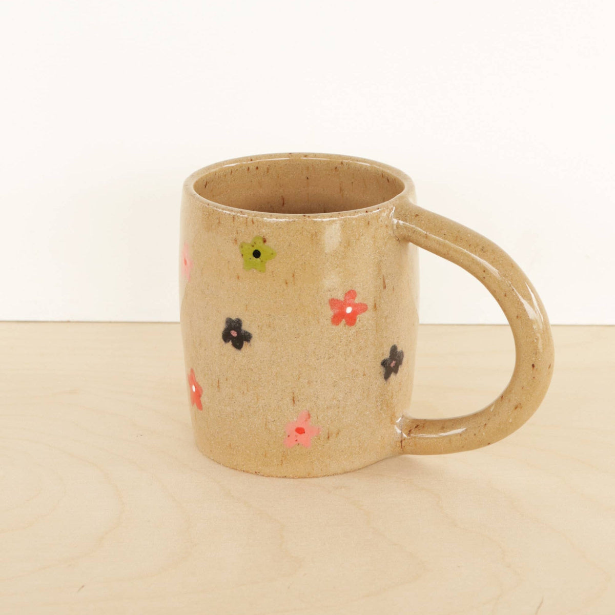 Beige ceramic mug with colorful floral patterns on a beige surface