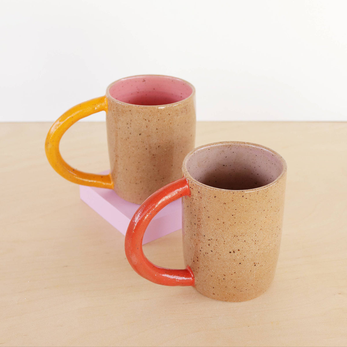 Two ceramic mugs with colorful handles on a beige background