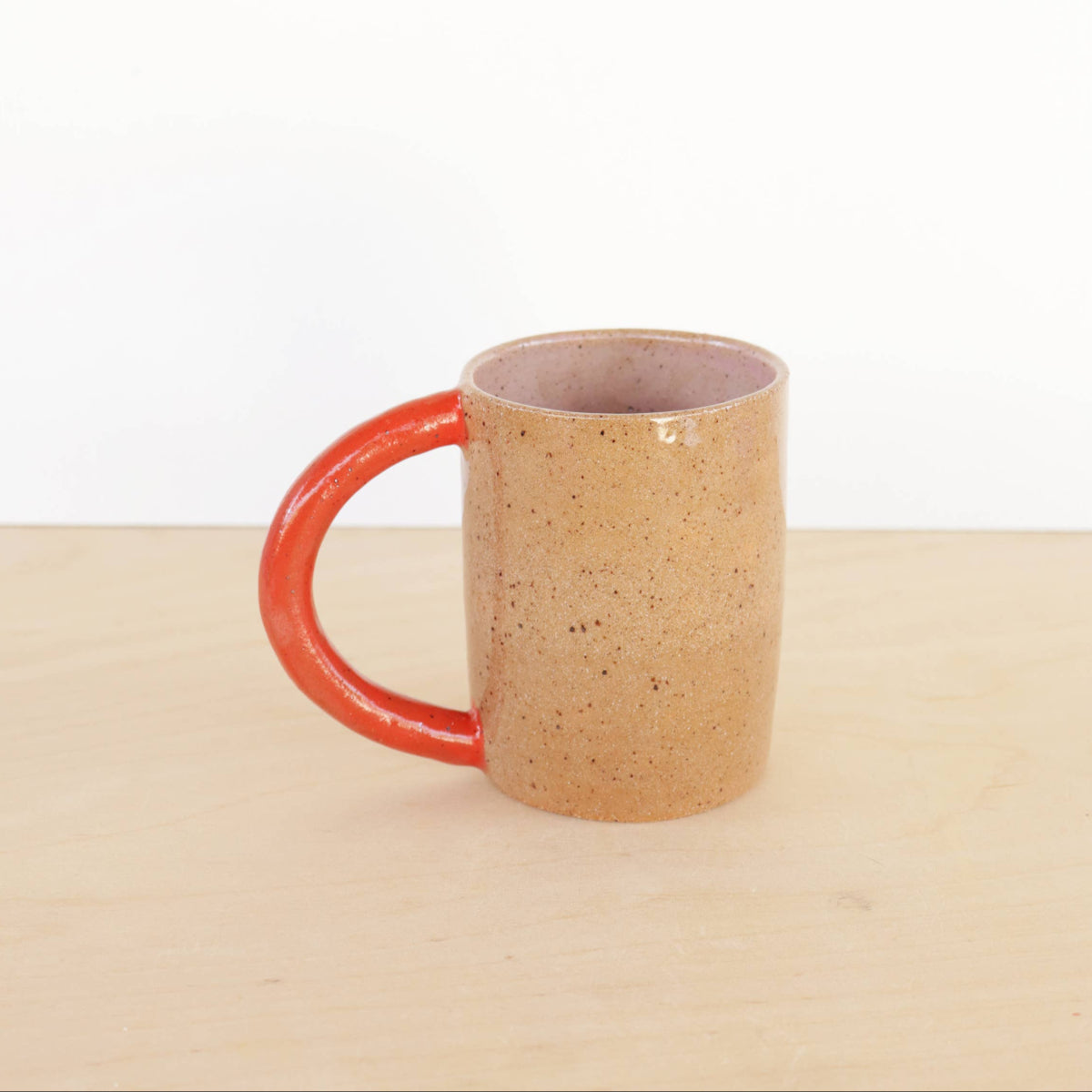 Speckled ceramic mug with red handle on a beige surface