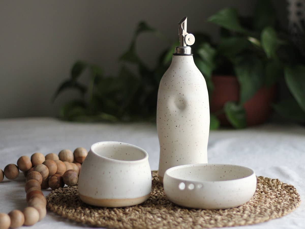 Calgary Clay Co. ceramic oil cruet in speckled white with thumb grip and stainless steel pouring spout, styled. Handmade in Canada.
