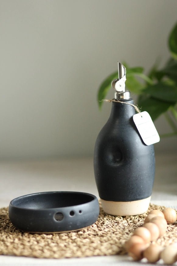 Calgary Clay Co. ceramic oil cruet in satin black with thumb grip and stainless steel pouring spout, styled. Handmade in Canada.