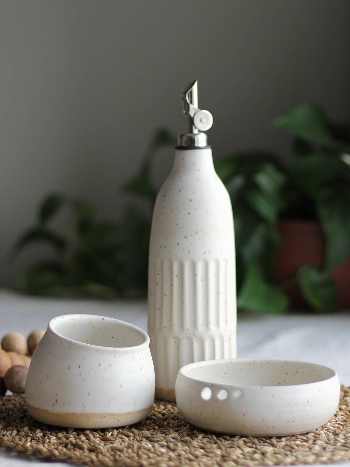 Calgary Clay Co. fluted ceramic oil bottle in speckled white glaze with a stainless steel gravity pouring spout, stylized.