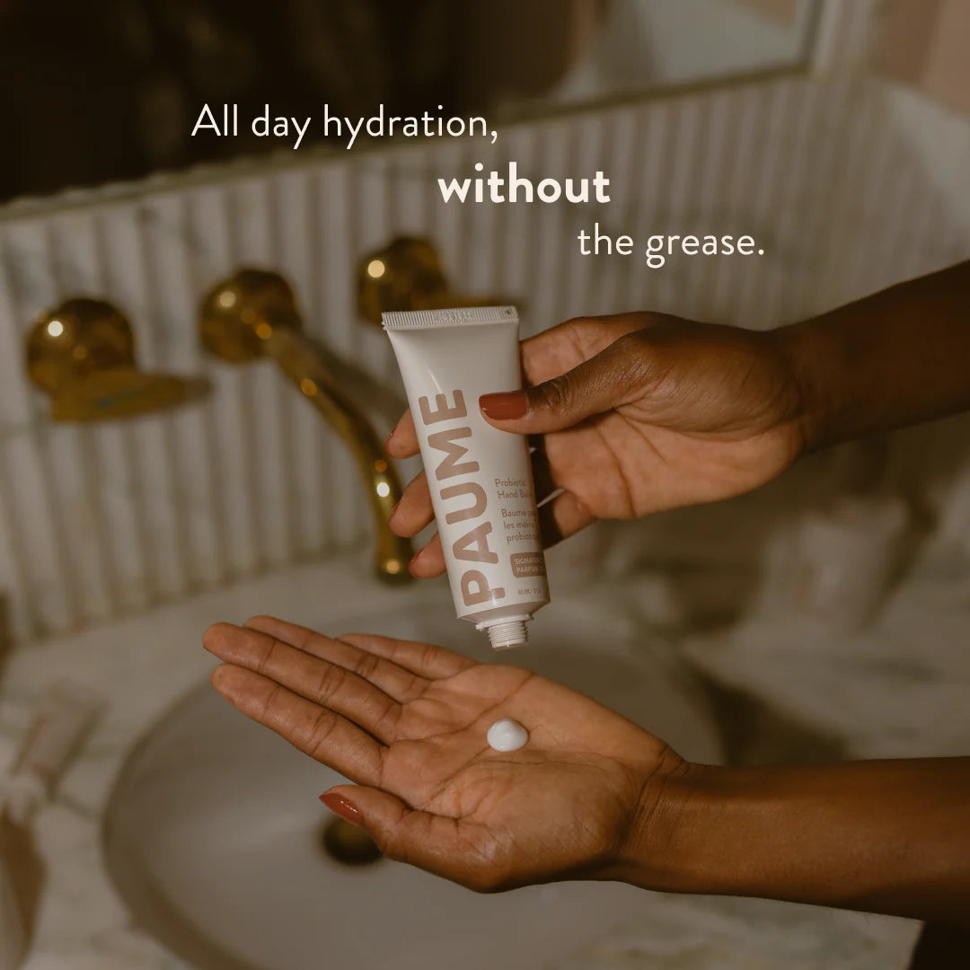 Hand holding a tube of PAUME cream with text about hydration in a bathroom setting