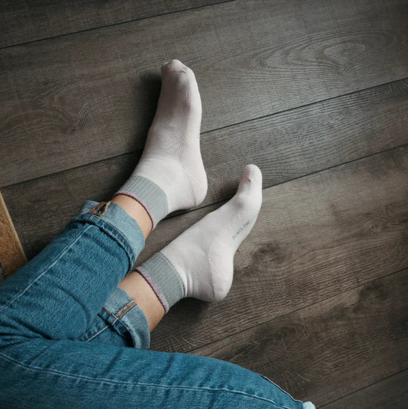 Feet wearing gray socks and blue jeans on a wooden floor