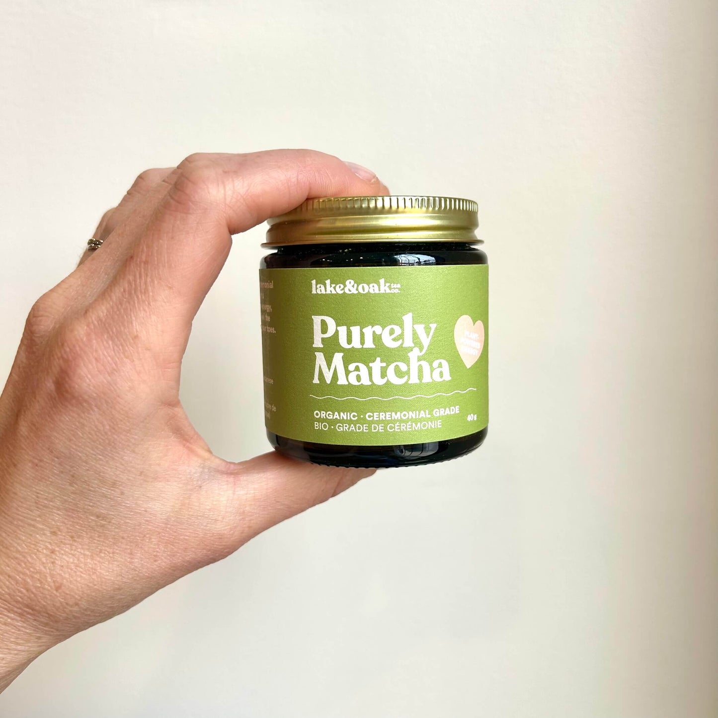 Hand holding a jar of 'Purely Matcha' by lake&oaks against a plain background