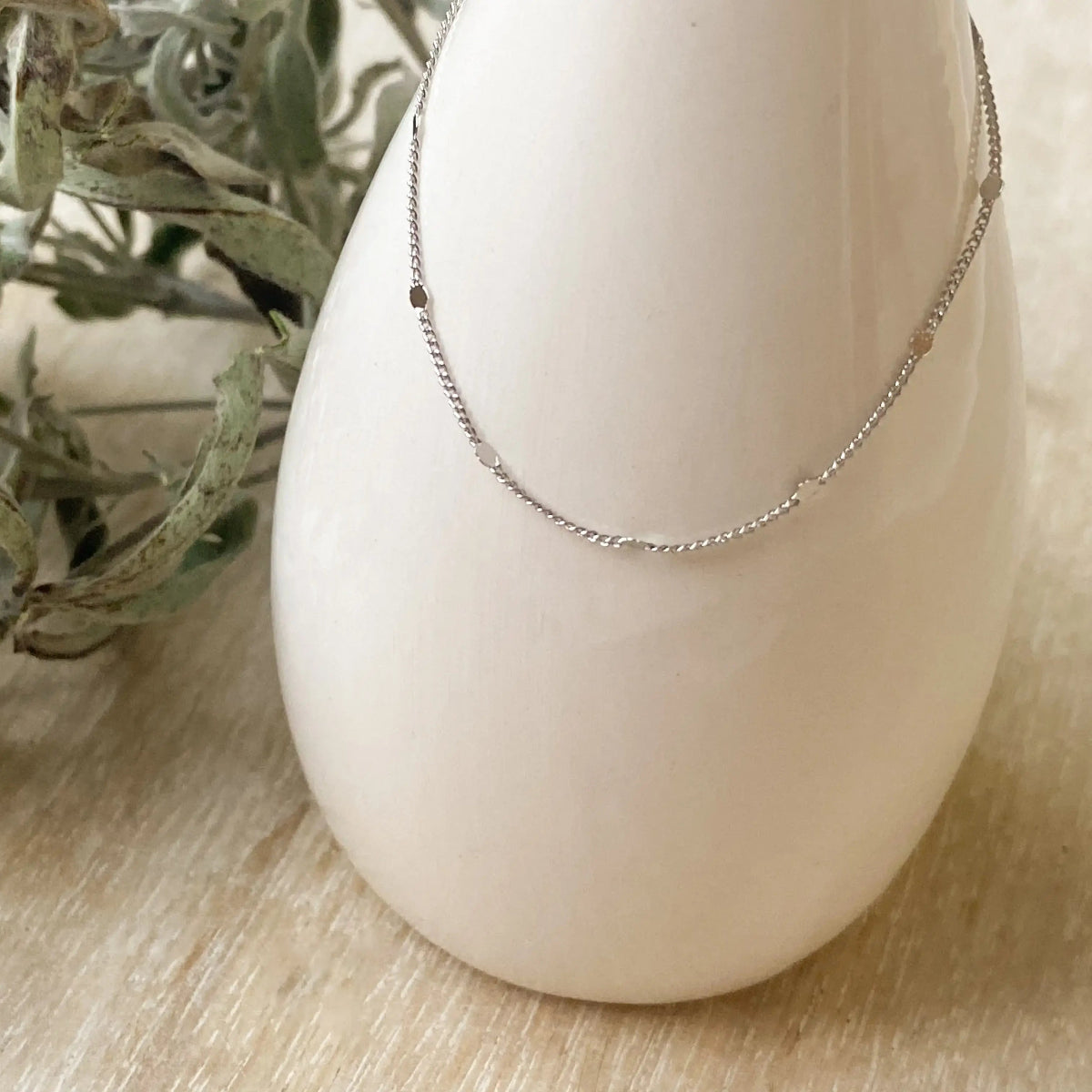 Silver necklace on a white stand with dried greenery in the background